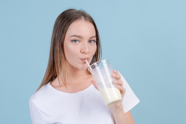 Cute caucasian young girl in white tshirt and striped pants drinks milkshake