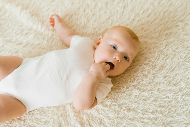 Cute charming white Caucasian boy with blue eyes lying on the bed smiling at the camera View from above A happy lifestyle in childhood