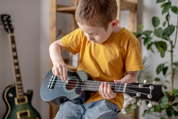 Cute cheerful boy is playing the ukulele in the music room Joyful learning to play musical instruments Hawaiian guitar