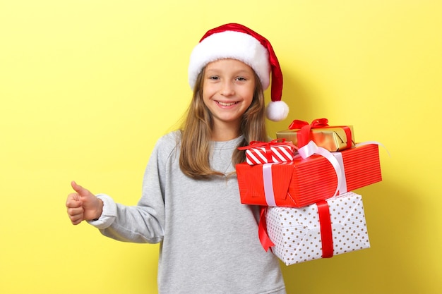 Cute cheerful girl in a christmas hat on a colored background holding a gift