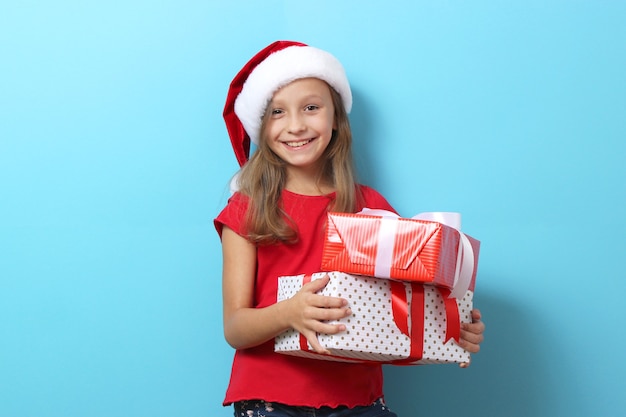 Cute cheerful girl in a christmas hat on a colored background holding a gift