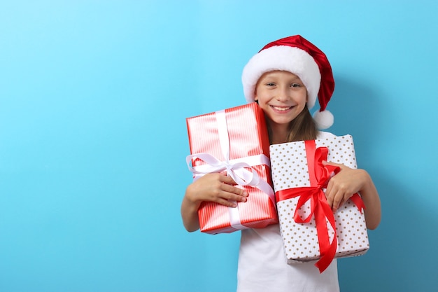 Cute cheerful girl in a christmas hat on a colored background holding a gift