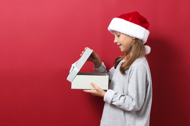 Cute cheerful girl in a christmas hat on a colored background holding a gift