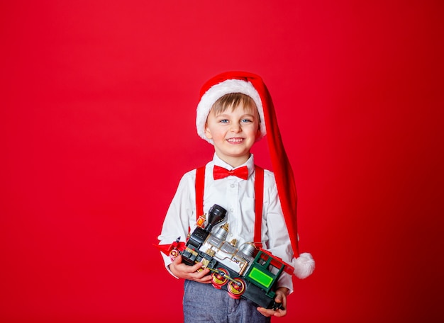 Cute cheerful little boy in Santa Claus hat on red