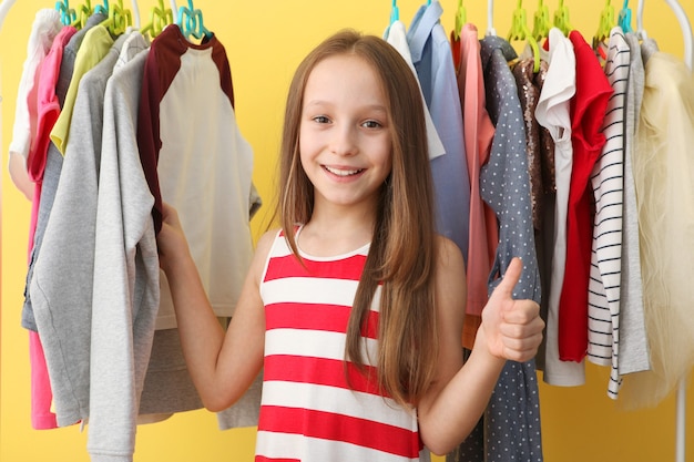 Cute cheerful little girl chooses clothes with floor hangers