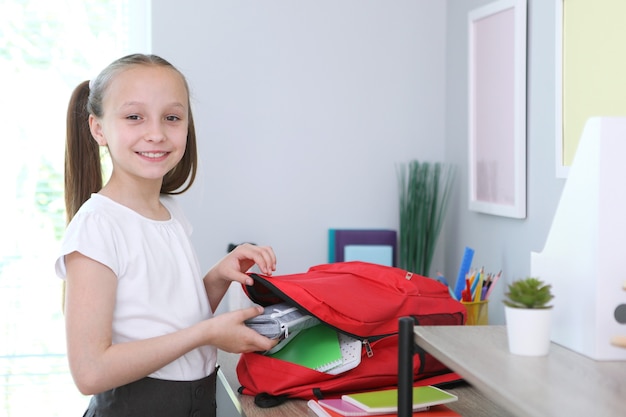 Cute cheerful schoolgirl puts stationery in a backpack