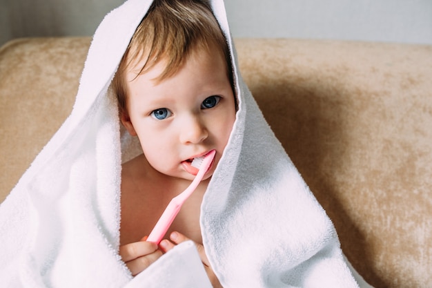 Cute child in big white towel she brushes his teeth with toothbrush