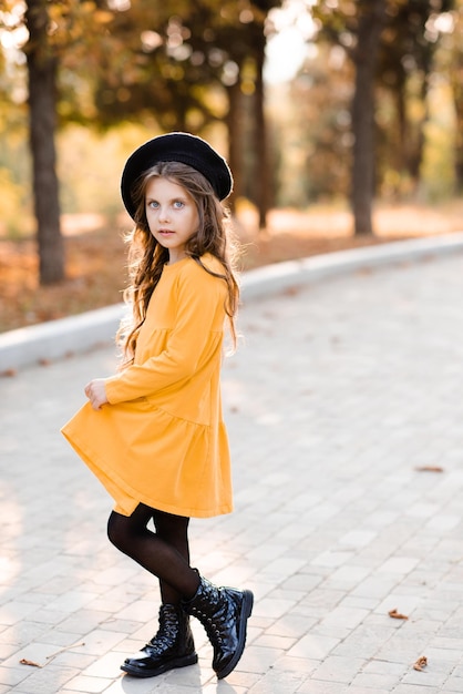 Cute child girl 5-6 year old wear yellow dress and beret walk on city street over autumn nature