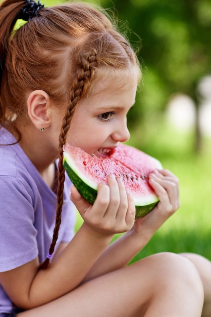 Cute child girl eats a watermelon in sunny summer day