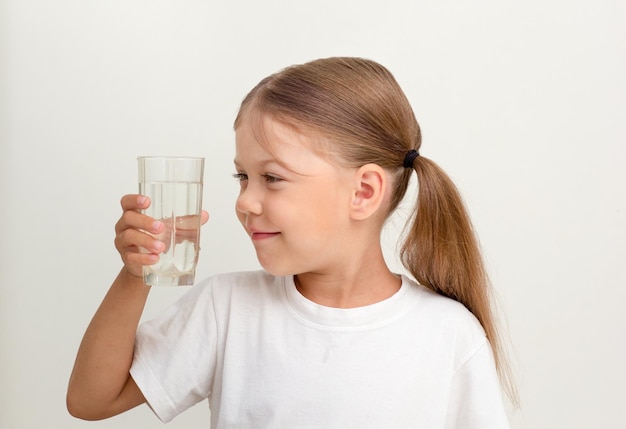 Cute child looking at glass of water in her hand on gray background