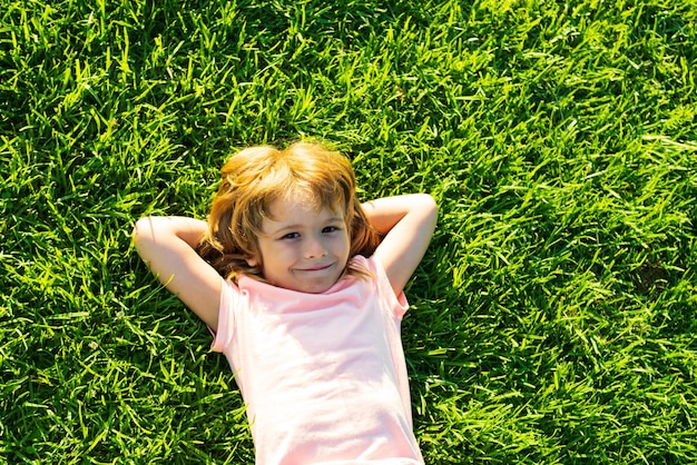 Cute child lying on grass background. Happy freedom kid boy enjoying on field and dreaming. Unity with nature.