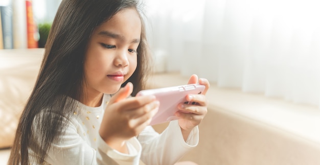 Cute child using a smartphone and smiling while sitting on sofa at home 