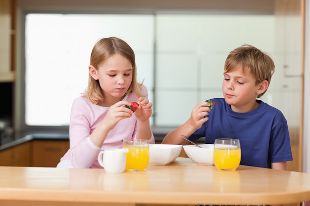 Cute children eating strawberries for breakfast