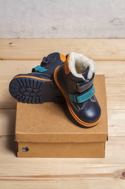 Photo cute children's autumn boots in a cardboard box on a wooden floor.