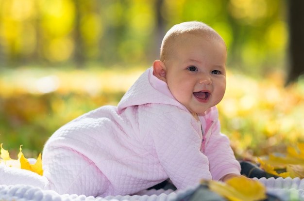 Cute chubby little baby girl laughing at camera as she crawls on a rug on the grass in an autumn park