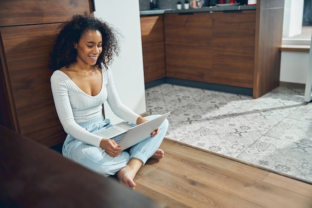 Cute contented young female freelancer staring at the computer on her knees