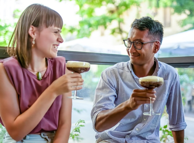 Cute couple flirting and enjoying carefree moment, two young people drinking shaked coffee at restaurant, date between young man and woman created by dating sites and app