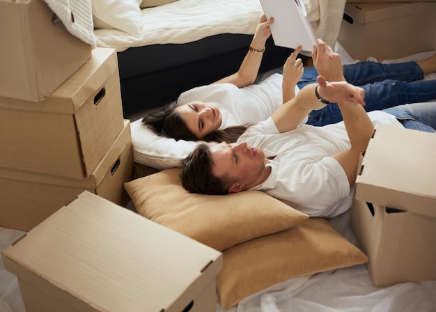 Cute couple unpacking cardboard boxes in their new home lying on the floor and looking at a family album