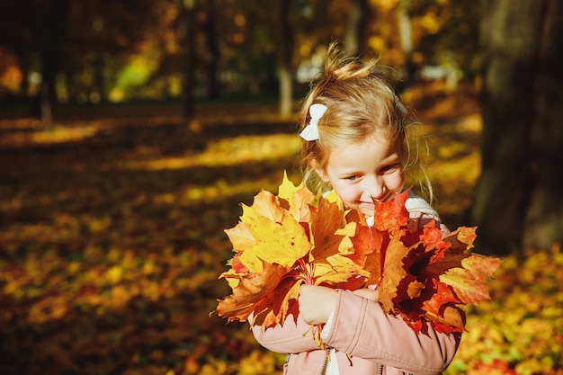 cute curly girl. Little funny girl playing with yellow leaves in the forest. Golden autumn. toddler girl, portrait with bouquet of autumn leaves