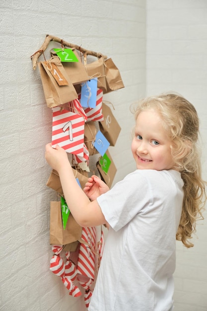 Cute curly girl with blond hair and a girl and an anvent calendar hanging on the wall the eve of christmas