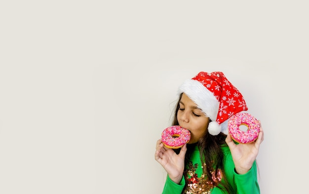 Cute dark hair girl in santa hat smiling, having fun and tasting two donuts on her eyes.