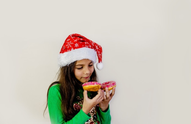 Cute dark hair girl in santa hat smiling, having fun and tasting two donuts on her eyes.