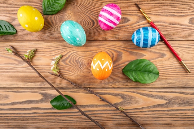 Cute Easter eggs decorated handmade with paint and paintbrush on a wooden background with green leaves and young branches