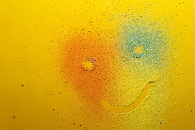 Cute emoticon that looks like a clown is drawn on a multicolored powder on a bright background