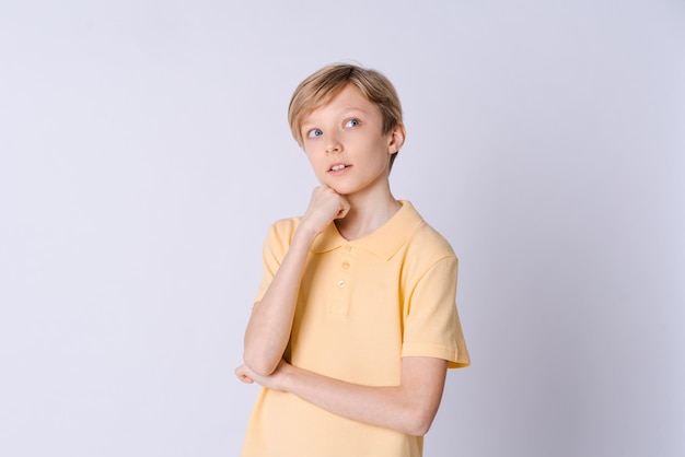 Cute emotional teenager boy in yellow tshirt posing in studio on light