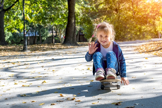 Cute female child sitting on a skateboard and playing in a park on a sunny day