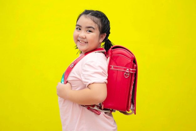 Cute female students and carrying a school bag Ice cream isolated on yellow background