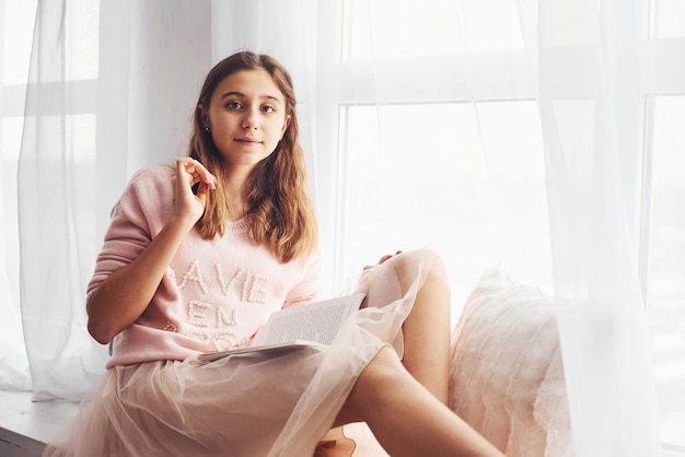 Cute female teen sits indoors in the living room with book at holidays time.