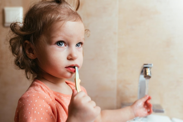 Cute and funny baby girl brushing her teeth in the morning in the bath