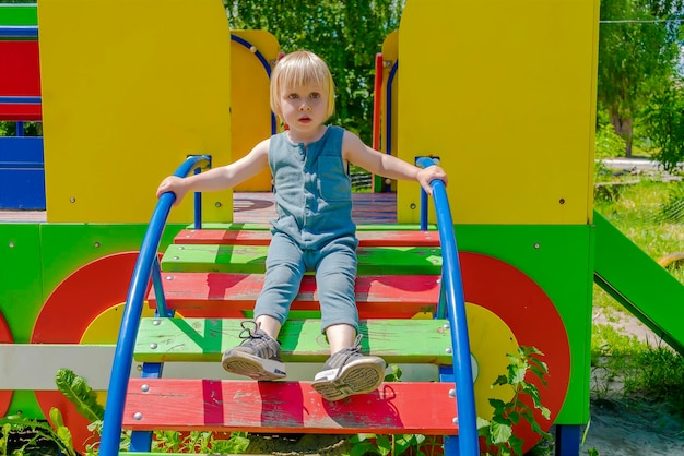 Cute funny blonde little young toddler kid child boy going down wooden ladderslide in playground Children physicalemotional development and childhood daycare kindergarten concept at summer