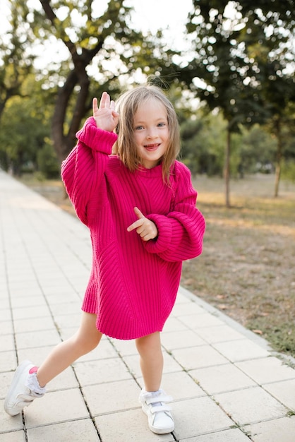 Cute funny child girl 4-5 year old wear bright pink sweater having fun playing in park outdoor