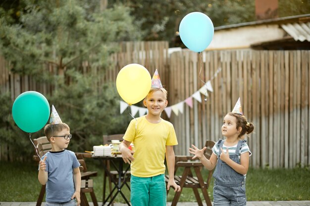 Cute funny kids celebrating birthday with family or friends in a backyard Birthday party Kid wearing party hat and launch balloons into the sky