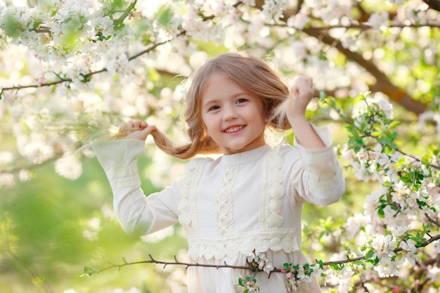 a cute funny little girl in a dress in spring near a flowering tree is laughing gentle photography