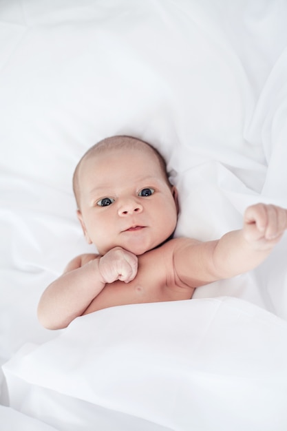 Cute and funny newborn baby boy awake in the bed