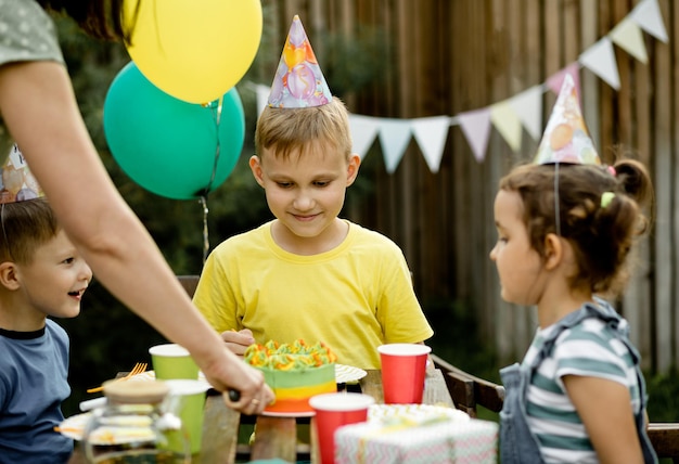 Cute funny nine year old boy celebrating his birthday with family or friends and eating homemade baked cake in a backyard Birthday party for kids