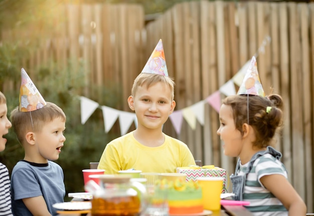 Cute funny nine year old boy celebrating his birthday with family or friends with homemade baked cake in a backyard Birthday party Kids wearing party hats