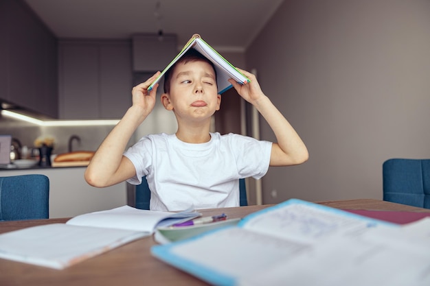 Cute funny small caucasian teen schoolboy holding book above head and mocking lazyhomework