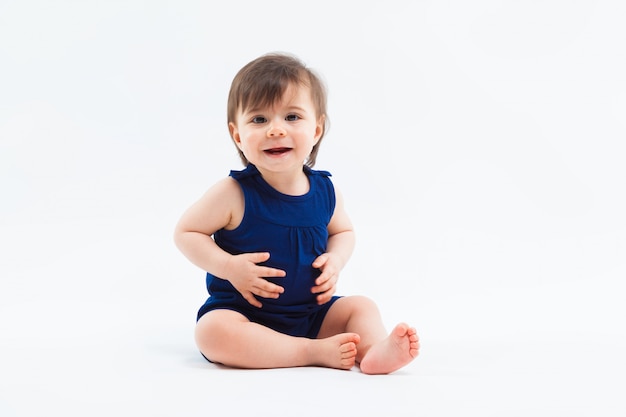 Cute funny small smiling girl sitting in studio posing on white background