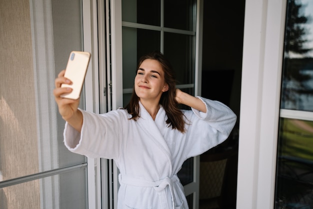 Cute girl in bathrobe takes selfie on balcony