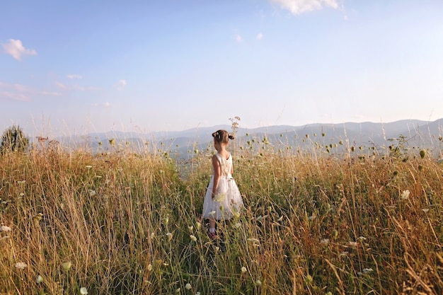 Photo cute girl dancing through a beautiful meadow with wheat and flowers in the mountains