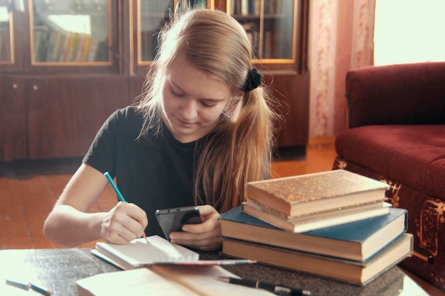 Cute girl doing homework writing and holds a smartphone