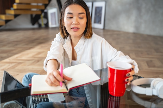 Cute girl drinking tasty beverage and looking at notebook