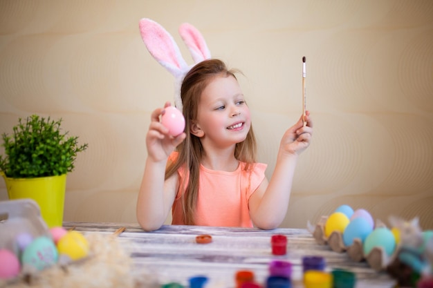 Cute girl in easter bunny ears painting easter eggs at home prepares to easter happy easter