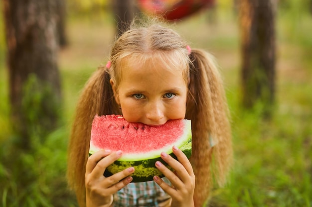 Cute girl eating watermelon at park in the forest