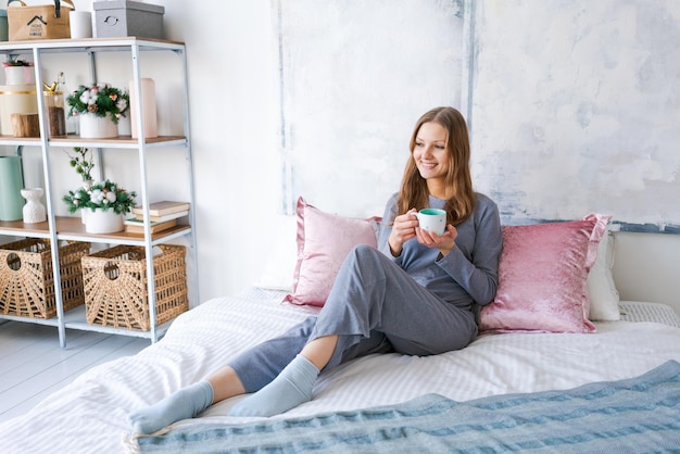 Cute girl enjoys coffee or tea in bed in morning in her pajamas Beautiful