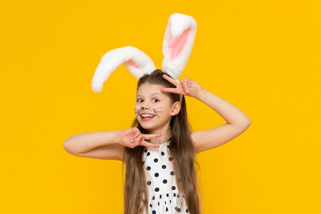 Cute girl in fancy Easter bunny ears and painted mustache on a yellow isolated background Easter spring holiday A girl in the ears of an Easter bunny